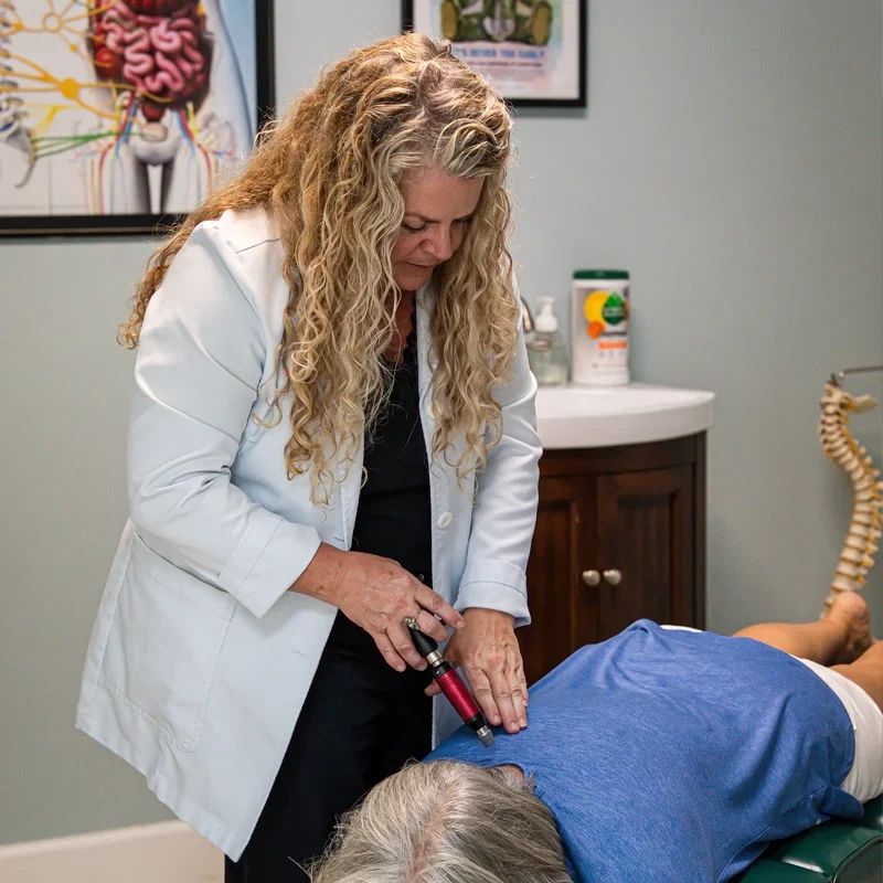 Joy McClenny using a handheld adjusting instrument on a patient’s upper back.